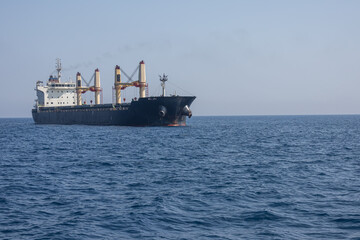 A large marine vessel transports cargo on the high seas. Navigation of large ships. A large cargo ship at sea. Smoke is coming out of the chimney of a marine vessel.