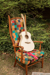 acoustic guitar leaning on a wooden vintage chair with vibrant patchwork upholstery, set outdoors