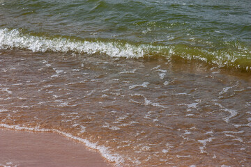 Soft wave of the sea on the sandy beach. Small waves on a sandy beach. The concept of summer, relaxation, and swimming