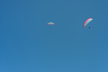 Two paragliders soaring in a clear blue sky on a sunny day