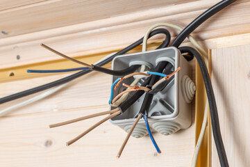 Open junction box with multiple exposed copper, blue, and brown wires ready for electrical installation inside wooden house.