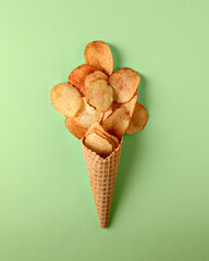 Unusual creative snack concept: crispy potato chips arranged in a waffle cone on light green background evoke playful, surprising mood.