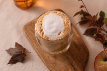 Maple apple latte with creamy foam in transparent cup on wooden board, autumn leaves and apple create cozy seasonal atmosphere.