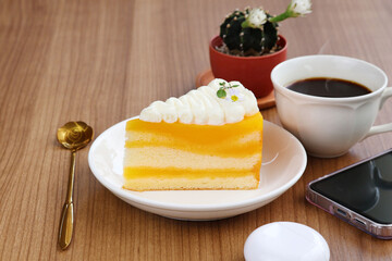 Hot black coffee and sliced cake with yellow accents sit on a wide, natural wooden table.

