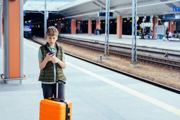 Teen boy with suitcase checking phone at train station