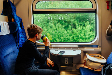 Teen boy drinking from yellow cup during train ride