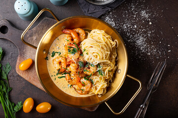 Pasta with shrimps in creamy sauce in a pan on dark background top view