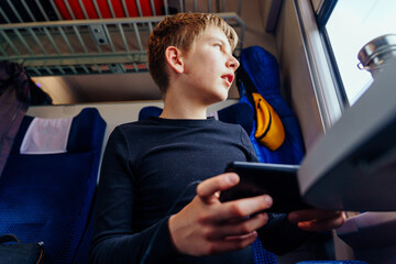 Teen boy with smartphone looking out train window