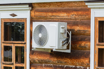 Modern air conditioner unit installed on the exterior wall of a rustic log house between vintage...