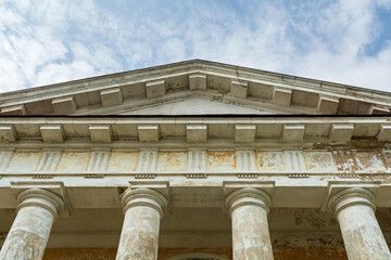 Aged neoclassical building with grand stone columns and weathered pediment stands against blue sky, echoing echoes of historic elegance.