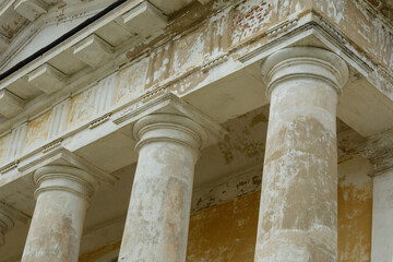 Three weathered neoclassical columns support an aged entablature, showing timeworn textures and...