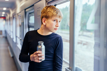 Teen boy holding bottle and looking through train window