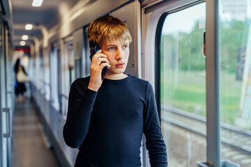 Teen boy talking on phone by train window