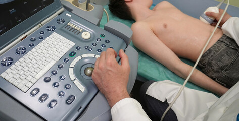 Fototapeta premium Ultrasound examination of a child in a medical office. The doctor uses the ultrasound sensor and the control panel of the device for diagnosis. The procedure takes place on a special couch.