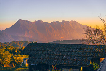 High-angle view of a beautiful orange, pink, and yellow sky in the evening as the sun sets. There is a view of Doi Luang Chiang Dao Mountain in the center of the image, which has a unique shape.