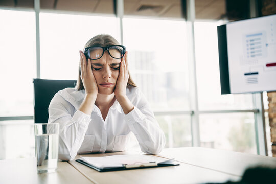 Stressed businesswoman in a modern office struggling with work pressure and challenges, seated at a desk in frustration - Powered by Adobe