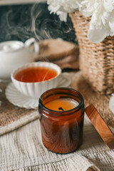 Close-up of an extinguished candle with smoke swirling in the air, next to a cup of tea and white flowers on a cozy linen surface. Warm, calm, relaxing atmosphere in natural tones