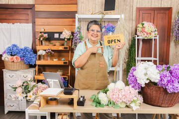 Asian senior woman, florist, small business owner proudly holds open sign with smile, ready to...