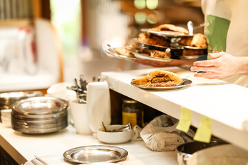 Traditional Balkan food being served in a restaurant kitchen, with fresh somun bread and grilled meat on metal plates, ready for customers in a lively local setting.