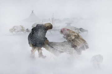 Yamalo Nenets, Russia - 16 April 2021: View of figures battling the fierce blizzard amidst a landscape of snow-covered yurts and indistinct forms.