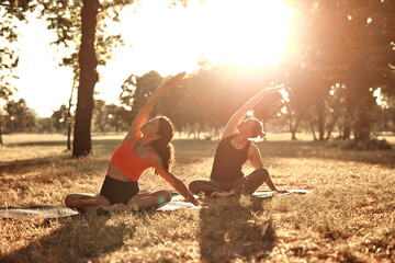 Two women practicing yoga and stretching in the park on a hot sunny summertime day.