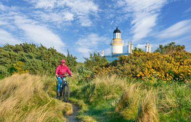 nice senior woman riding her electric mountain bike between blooming gorse i at Chanonry Point...