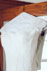 Elegant white lace wedding dress hanging in a bright room ready for a special day
