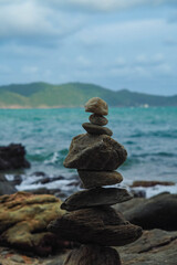 A stack of balanced rocks stands on a shore, with the ocean and distant mountains visible in the background.