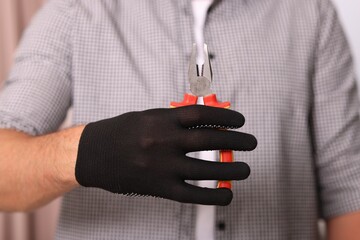 Man in glove holding pliers indoors, closeup