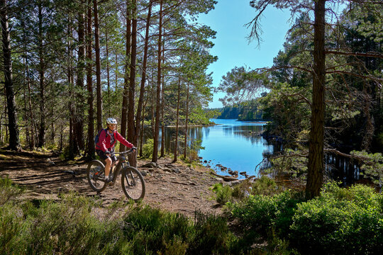 nice senior woman riding her electric mountain bike at Loch An Eilein in the Cairn Gorms National Park near Aviemore Scotland, UK