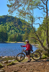 Obraz premium nice senior woman riding her electric mountain bike at Loch An Eilein in the Cairn Gorms National Park near Aviemore Scotland, UK