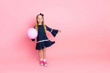 Smiling young girl holding pink balloon against solid background wearing casual fashionable dress and sporting happy expression © deagreez