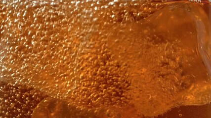 Captivating close up of sparkling golden amber liquid with energetic effervescent bubbles and submerged ice a refreshing cool beverage texture background - Powered by Adobe