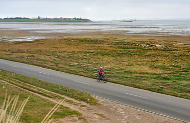 woman with elctric mountain bike crossing the Causeway to Holy Island and Lindisfarne, in Northumbria, England, UK