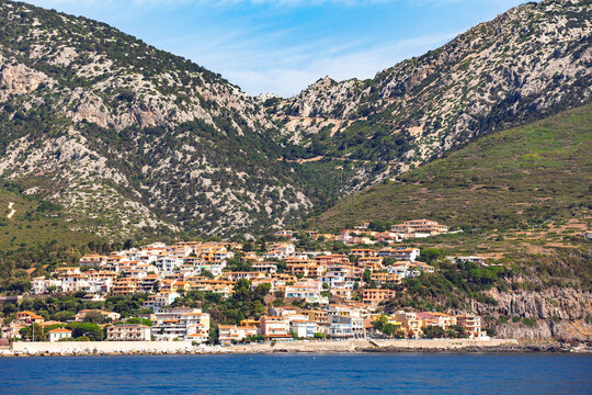 Colorful coastal town nestled at the base of rugged green mountains along rocky shoreline