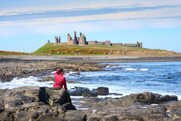 woman admiring medieval ruin of Dunstanburgh castle in north eastern England, UK