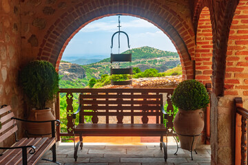 Wooden bench framed by brick arch overlooking green mountains in Meteora Greece