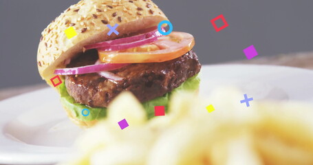 Sesame seed bun burger sitting on white plate in studio with fries, floating shapes, copy space