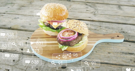 Displaying sesame bun burgers on wooden board with blue handle at picnic table, with media icons