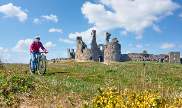 nice senior woman cycling with her elctric mountain bike at Dunstanburgh castle in north eastern England, UK