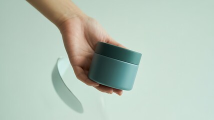A person s hand gently holds a stylish teal colored reusable coffee cup against a soft light background