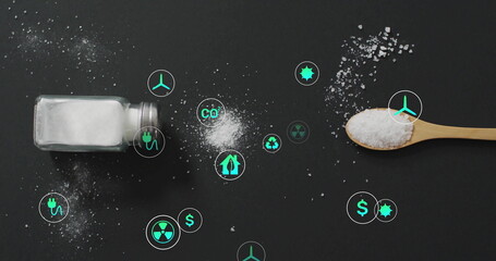 Spilling granules from glass shaker, wooden spoon on dark tabletop with neon cyan icons, copy space