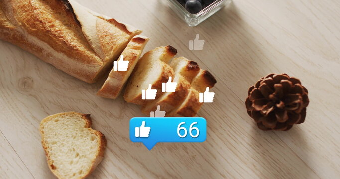 Showing sliced baguette lying on table with blueberries, pinecone, thumbs-up icons and like bubble