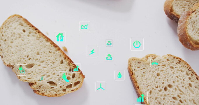 Displaying crusty artisan bread slices on white table with floating environmental icons and crumbs - Powered by Adobe