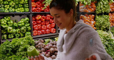 Inspecting woman examining green bell pepper in grocery store, with pepper crates, copy space