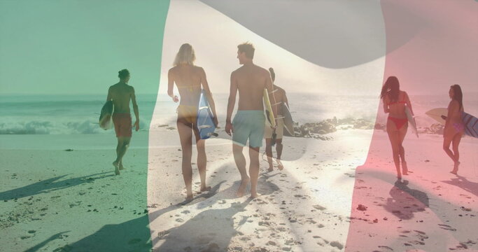 Walking group of six surfers carrying surfboards across wet sand toward ocean, sunset light