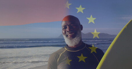 Standing man wearing wetsuit holding yellow surfboard at shore, with EU stars overlay