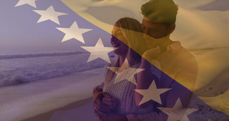 Smiling couple embracing each other on sandy beach at sunset, with Bosnian flag overlay