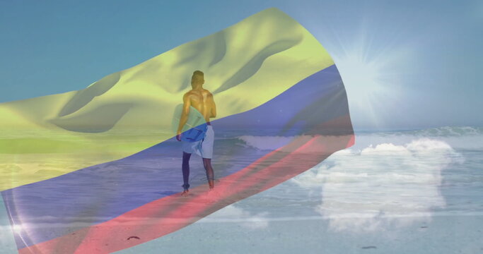 Standing shirtless traveler wearing blue shorts on beach with Colombian flag and blue backpack - Powered by Adobe