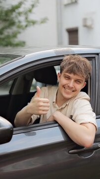 Smiling young man driver showing thumbs up and smiling at camera in car. Vertical video.